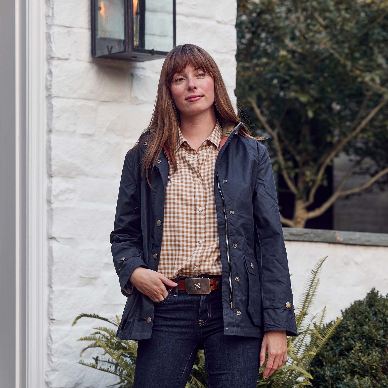 Woman outdoors in a Tom Beckbe Womens Smyth Cotton Twill Shirt, by a white brick wall with greenery nearby.