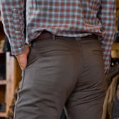 Seen from behind, a person wears Tom Beckbe Stafford Double Front Pants and a plaid shirt, hand in their pocket.