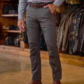 Man wearing Tom Beckbe Stafford Double Front Pant and plaid shirt stands in store with jackets in background.