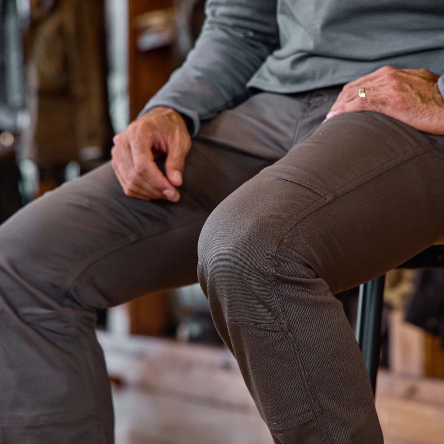 A person in a gray long-sleeve shirt wears Tom Beckbe's Stafford Double Front Pant while seated on a stool.