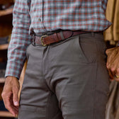 A person wearing Tom Beckbe Stafford Double Front Pant with a plaid shirt and brown belt, standing indoors.