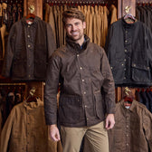 Man wearing a Tom Beckbe Tensaw Jacket stands in a store with shelter cloth jackets hanging behind him.