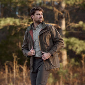 A man in a Tom Beckbe Tensaw Jacket stands outside in a forest.