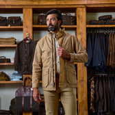 A man wearing a Tom Beckbe Tensaw Jacket stands in a clothing store with shelves of bags and hanging clothes behind him.