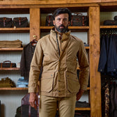 Man wears a Tom Beckbe Tensaw Jacket made from durable shelter cloth, standing by shelves with folded clothes and bags.