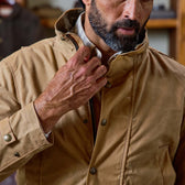 A man zips up a Tom Beckbe Tensaw Jacket, highlighting its high collar, bearded face, and durable shelter cloth.