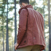 A person in a Fox Red Tensaw Jacket by Tom Beckbe stands outside with tall trees in the background.