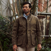 A man in a Tom Beckbe Tensaw Jacket stands indoors among plants, looking to the side with a neutral expression.
