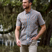 In a wooded area, a man smiles in Tom Beckbes Tidewater Shirt (Short Sleeve) and pants.