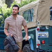 A man in a Tom Beckbe Tidewater Shirt (Short Sleeve) and backpack stands beside a vintage jeep with a South Carolina plate.
