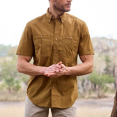 Man wearing a Tom Beckbe Tidewater Shirt (Short Sleeve) in brown, standing outdoors against blurred trees.