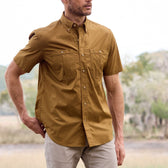 Man outdoors in a Tom Beckbe Tidewater Shirt, short sleeve and brown, featuring two chest pockets against a nature backdrop.