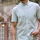 Person in Tom Beckbes Tidewater Shirt, short-sleeve light blue with UPF 30+, stands by a brick building.