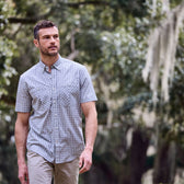 Man wearing a Tom Beckbe Tidewater Shirt walks outdoors among trees with hanging moss.