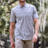 Man in a Tidewater Shirt by Tom Beckbe and beige pants, standing outdoors with trees in the background.