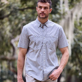 A man in a Tom Beckbe Tidewater Shirt strolls outdoors with trees in the backdrop.