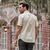 Man in Tom Beckbe Tidewater Shirt, facing away near a red brick building with large windows.