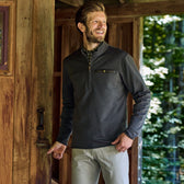 Man in a Tom Beckbe Tucker Fleece Quarter Zip smiles beside an open wooden door, with a forest in the background.