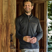 A man wearing a Tom Beckbe Tucker Fleece Quarter Zip smiles at a wooden doorway, with thermal insulation.