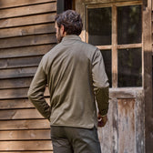 Man in Tom Beckbes Tucker Fleece Quarter Zip stands by a windowed door and insulated wooden wall.