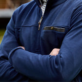 A person in a blue Tom Beckbe Tucker Fleece Quarter Zip with thermal insulation, arms crossed, stands outdoors.