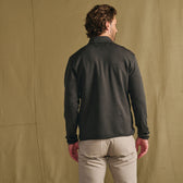 Man with brown hair in Tom Beckbe Tucker Fleece Quarter Zip, light pants, back to camera, tan backdrop.