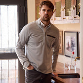 Man stands by a wooden bar counter wearing a Tom Beckbe Tucker Fleece Quarter Zip, near framed pictures on the wall.