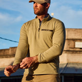 A person wearing a beige cap and Tom Beckbes Tucker Fleece Quarter Zip adjusts their sleeve outdoors against a blue sky.