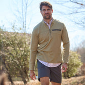 Man in a beige Tom Beckbe Tucker Fleece Quarter Zip over a checkered shirt and navy shorts, with trees behind him.