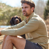 A man in a Tom Beckbe Tucker Fleece Quarter Zip sits outdoors with a brown dog, both gazing intently in the same direction.