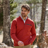 Man in a red Tom Beckbe Tucker Fleece Quarter Zip outdoors, trees in the background.