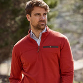 A person in a red Tom Beckbe Tucker Fleece Quarter Zip stands outside, glancing right, with blurred trees behind.