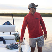 Man in a Tom Beckbe Tucker Fleece Quarter Zip stands on a boat, holding the rail. A shoe and items are on the seat.