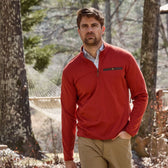 A man in a red Tom Beckbe Tucker Fleece Quarter Zip and khaki pants strolls outdoors, with trees and a hammock in view.