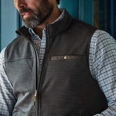 A man wearing a gray zip-up vest over a white plaid shirt stands in front of a blue door.