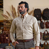 Man wearing the Tom Beckbe Uplander Shirt stands in store with bags and backpacks displayed behind him.