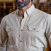 Man wearing the Tom Beckbe Uplander Shirt in beige oxford weave with two chest pockets, standing indoors.