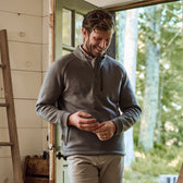 A man in a gray Tom Beckbe Warren Fleece Quarter Zip smiles by an open door, sunlight filtering through the woods.