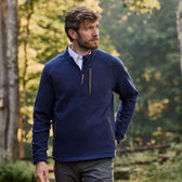A man wearing a Tom Beckbe Warren Fleece Quarter Zip stands outdoors in the woods, looking to the side with one hand in his pocket.
