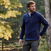 Man outdoors in blue Tom Beckbe Warren Fleece Quarter Zip and gray pants near a wooden fence with trees behind.