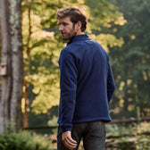A man in a navy Tom Beckbe Warren Fleece Quarter Zip stands outdoors with trees and morning light behind him.