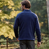 A man in a blue sweater and gray pants, outdoors by trees and a fence, wears a Tom Beckbe Warren Fleece Quarter Zip.