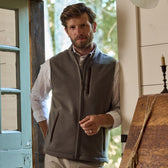 Man in a Tom Beckbe Warren Fleece Vest and checkered shirt by an open door, indoors, with natural light streaming in.