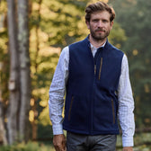 Man in a Tom Beckbe Warren Fleece Vest and checkered shirt walking through a sunlit forest.