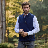 A man in a checkered shirt and Warren Fleece Vest by Tom Beckbe stands outdoors adjusting his sleeve, trees in the background.