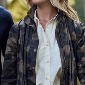 Wearing a Womens Blakeley Jacket by Tom Beckbe over a white shirt, a person strolls through blurred greenery with loose hair, capturing a casual and relaxed moment.