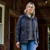 Someone wearing a Tom Beckbe Womens Blakeley Jacket and jeans stands by a wooden structure with a partially open door.