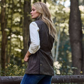 Long-haired person in Tom Beckbe Womens Fairmont Vest and jeans by a wooden fence in a forest.