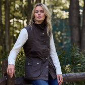 A person in a white shirt and a Tom Beckbe Womens Fairmont Vest stands by a wooden fence in a forest.
