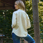 A woman in a Tom Beckbe Oxford Shirt and jeans leans on a wooden post amid lush greenery.